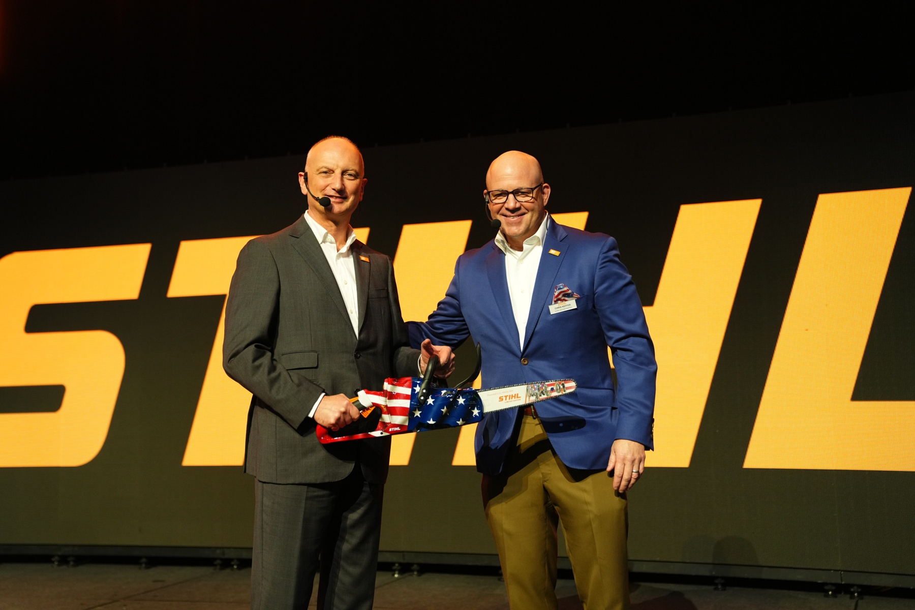Dr. Nikolas Stihl (à esquerda) e Chris Keffer, Diretor Geral da STIHL Inc. nos EUA, apresentam uma serra de aniversário com uma bandeira dos EUA.